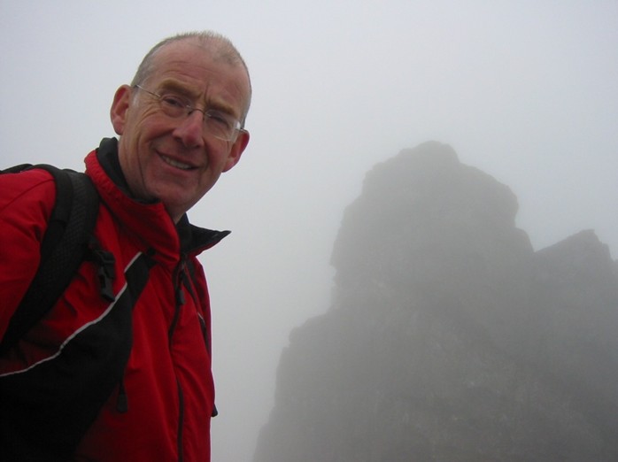 Dave Cherry on the summit of An Teallach with the summit cairn behind him.